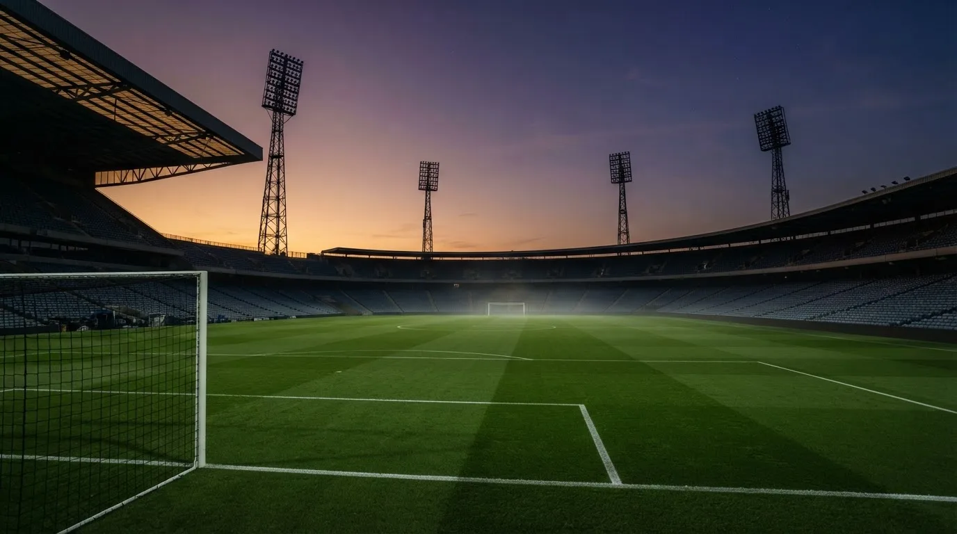 An empty football stadium with floodlight masts at dusk